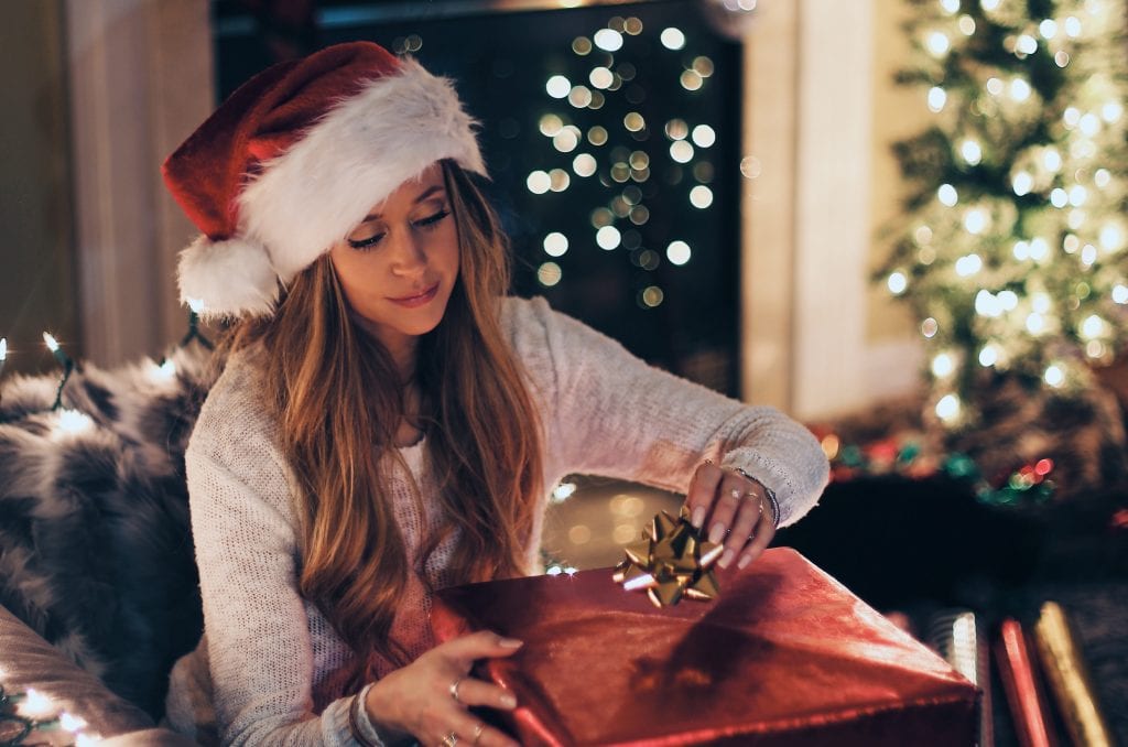 lady in santa hat opening up presents by a christmas tree
