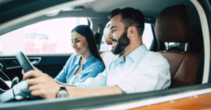 young couple test driving orange car smiling bearded blue shirt white people