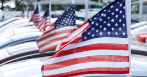 american flags on top of cars at a car dealership line of cars