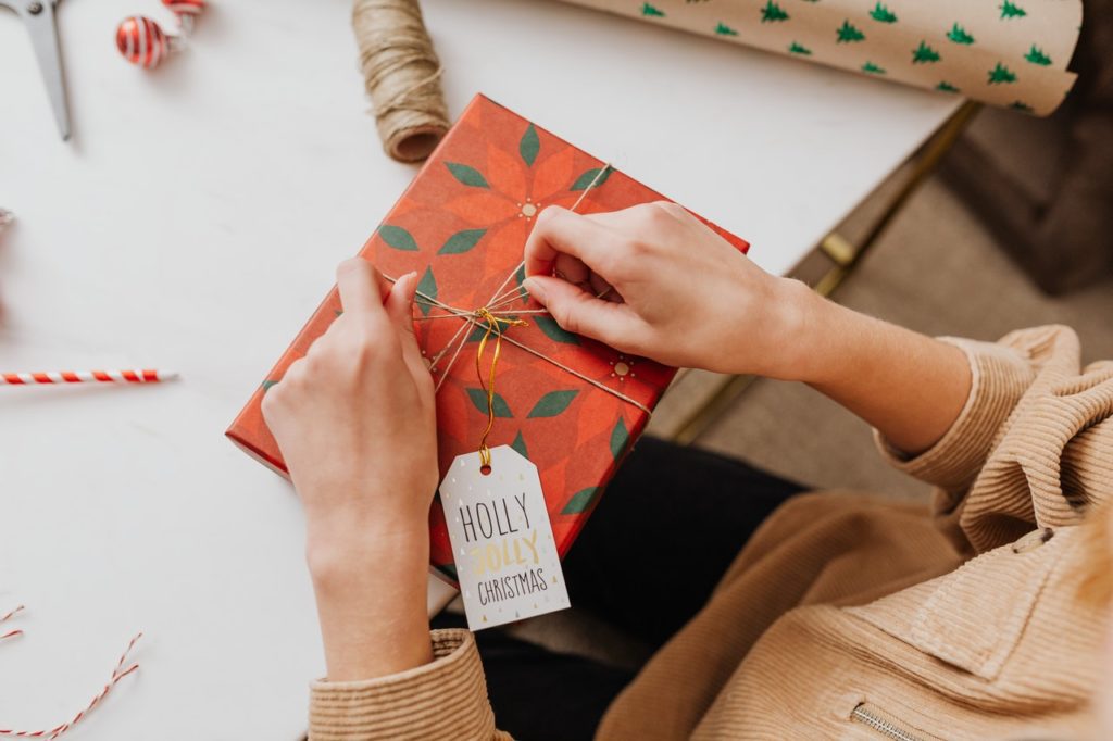 person wrapping a gift with festive paper and gift tag