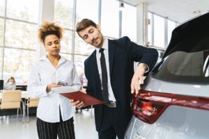 girl looking on as salesman shows off a car