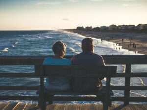 old couple sitting on a bench looking at ocean