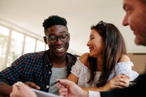 Happy interracial couple looking at their new house lease agreement and smiling with estate broker. Young couple renting a new house.
