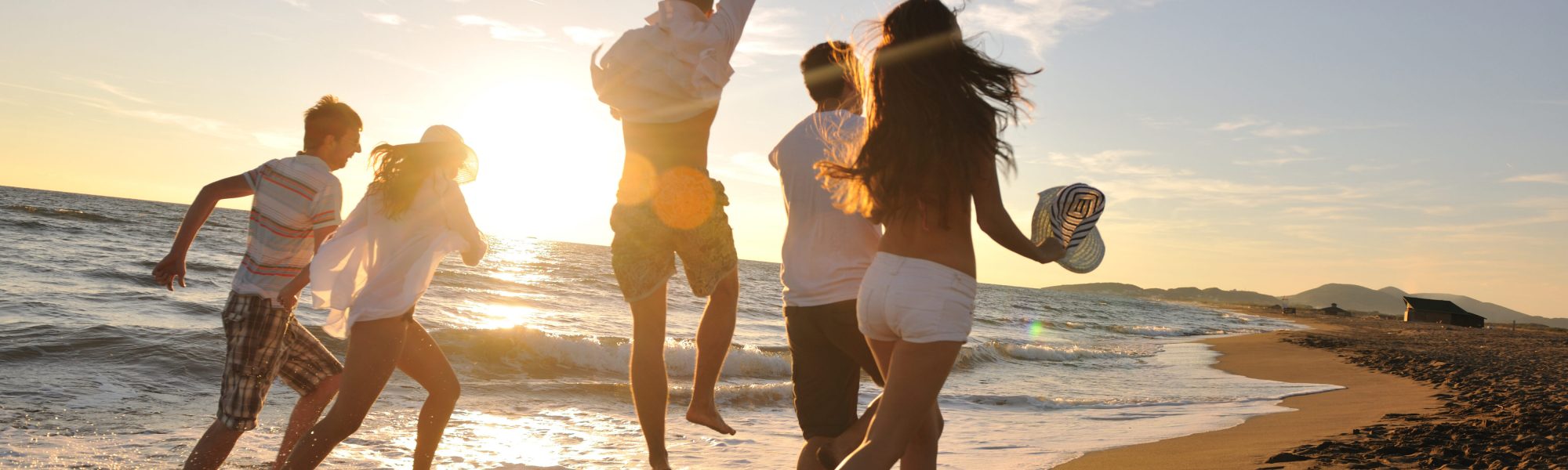 Happy young friends group have fun and celebrate while jumping and running on the beach at the sunset