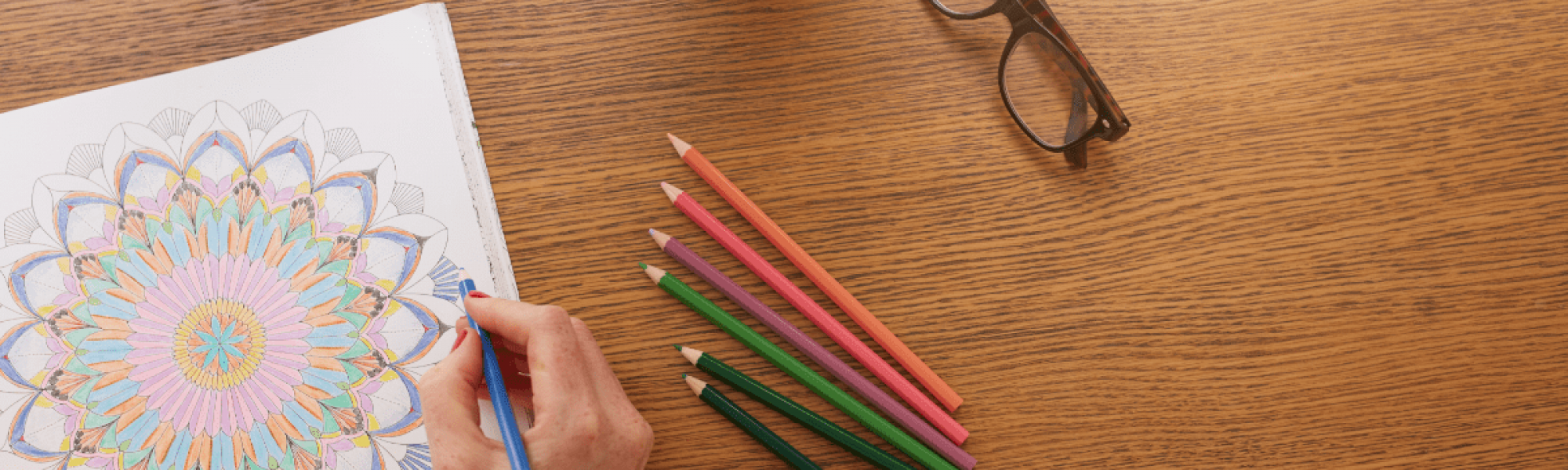 female hand coloring with colored pencils on a wooden table glasses